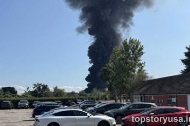 BREAKING NEWS large dark smoke plume rising from industrial fire in parking lot area with vehicles and buildings
